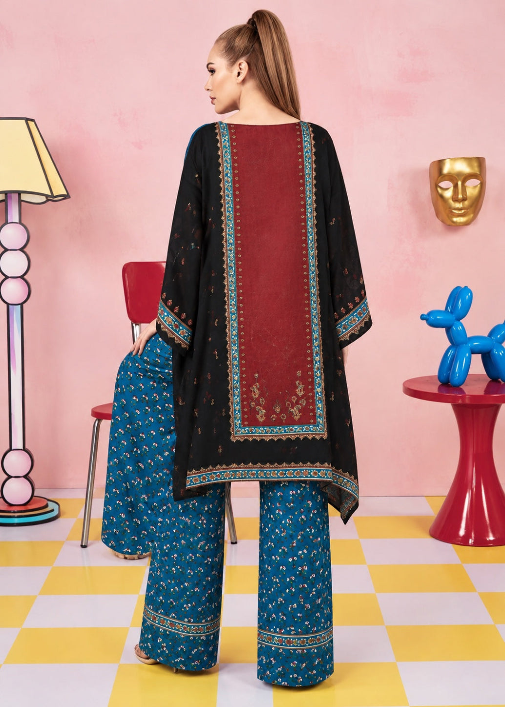 A woman stands with her back to the camera wearing a three-piece traditional outfit. The set includes a black tunic with a wide red center panel and teal border embroidery, paired with matching teal wide-leg pants and a teal dupatta draped over her shoulder.